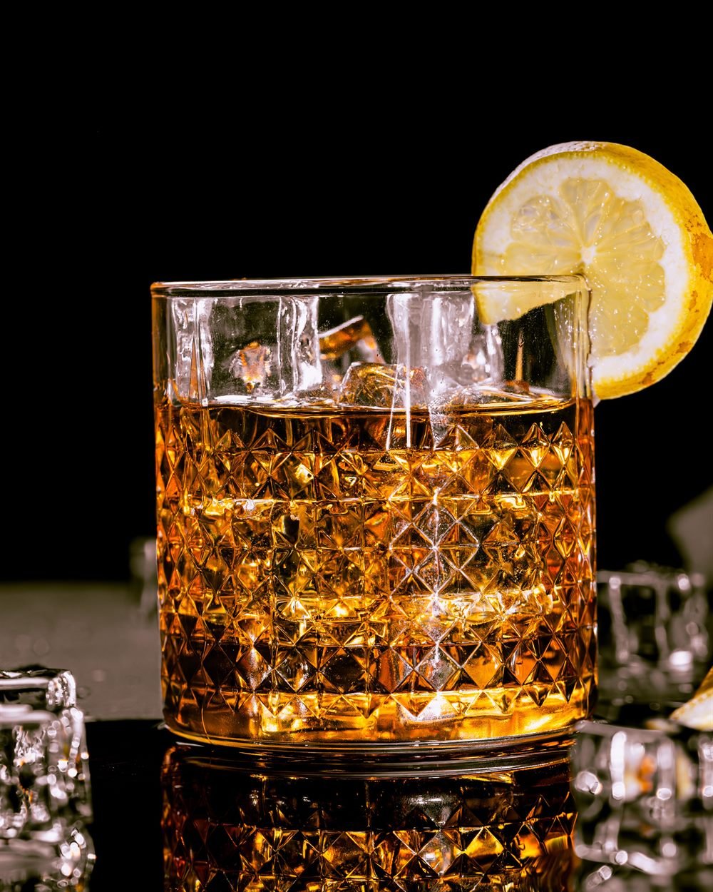 Whisky con hielo en vaso de cristal tallado sobre fondo negro