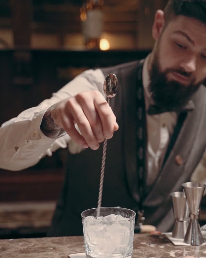 Bartender uniformado preparando un coctel con cuchara de bar en la barra